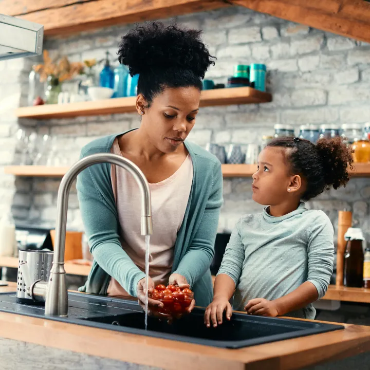 African American mother and daughter in kitchen cleaning tomatoes in sink