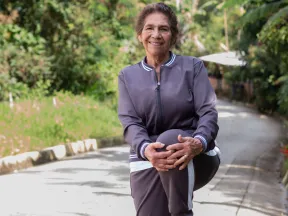 An older woman in a track suit stretches on one leg. 