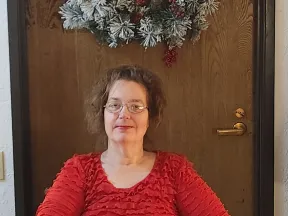 Photo of Christine sitting front of a door with a wreath.