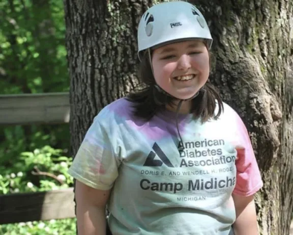 Smiling girl in a helmet, harness, and ADA Camp Midich t-shirt.
