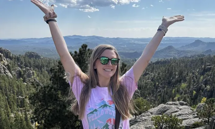 A woman on a mountain top with her arms raised.
