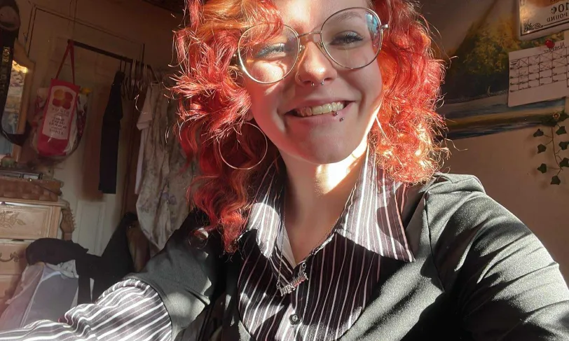 A selfie of a person with curly red hair and glasses smiling into the camera.