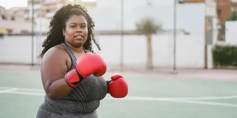 A curvy black woman wearing red boxing gloves ready to fight back obesity myths