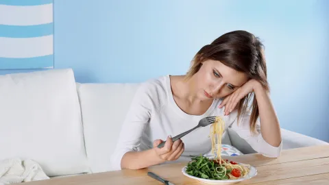 A sad woman stares at a plate of food. 