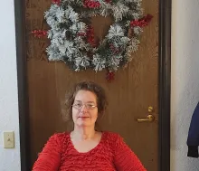 Photo of Christine sitting front of a door with a wreath.