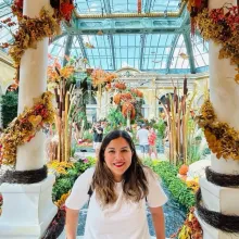 Woman smiles in an indoor garden decorated with autumn leaves and pumpkins.