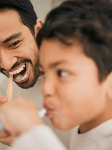 Happy Latino father and son brushing teeth together